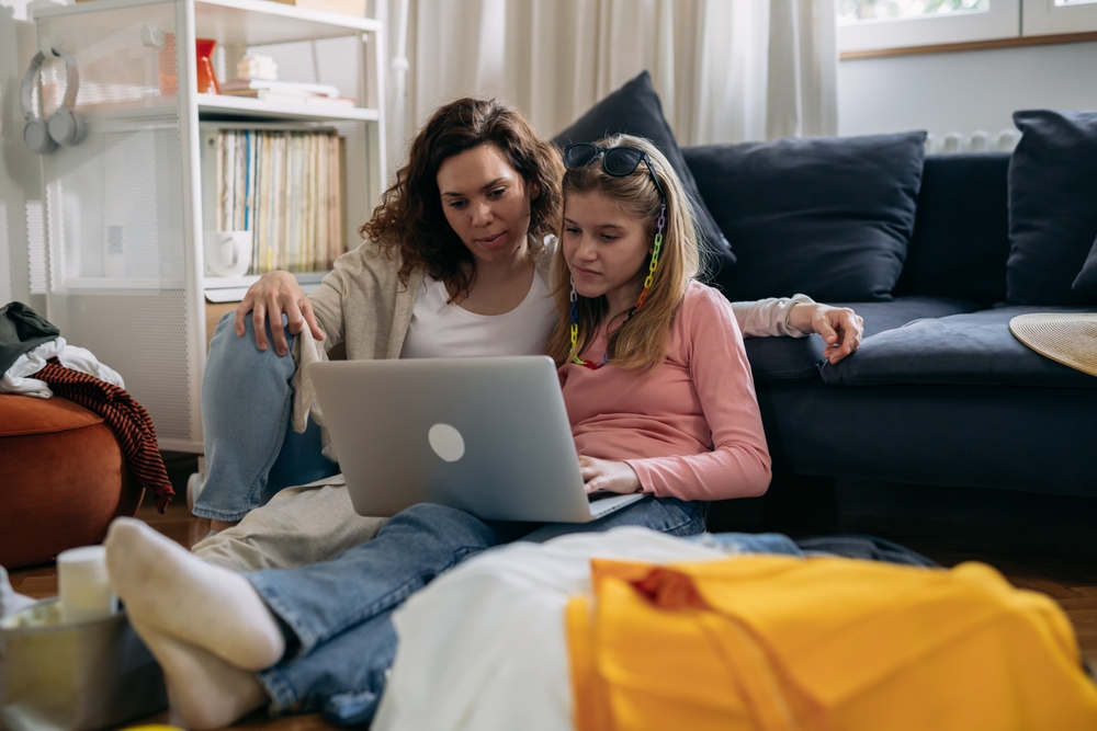 mother guides teen daughter on laptop, research 