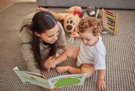 Mother, baby look at dinosaur book, baby holds toy dinosaur (How to Teach Children to Read at Any Age)