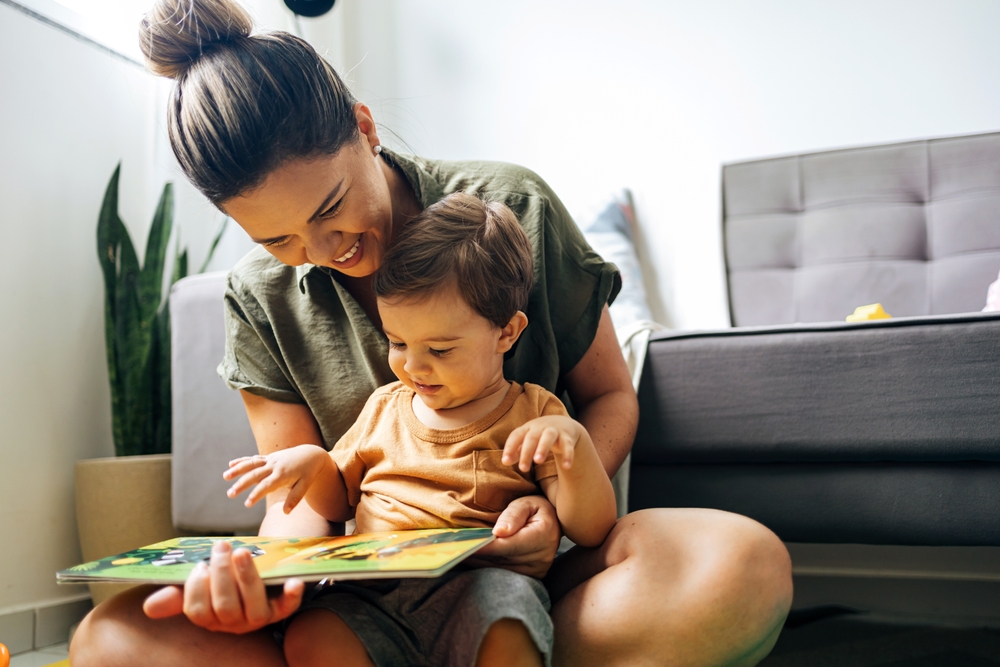 Toddler on mom's lap points to book as mom smiles (How to Teach Children to Read at Any Age)