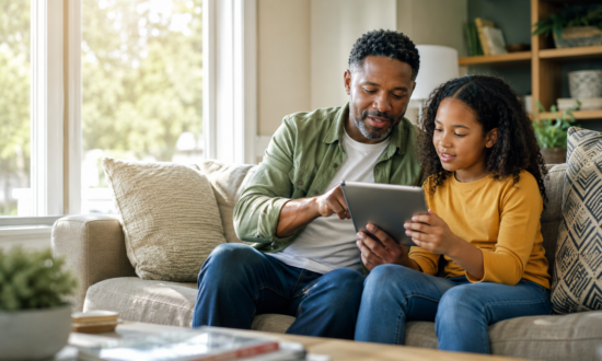 parent and preteen child sitting together on a comfortable living room couch looking at a tablet together.